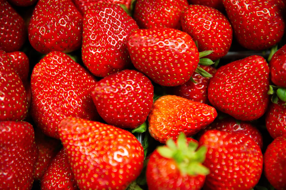 Close-up of many bright red strawberries with green stems, some with visible seeds.