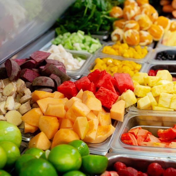 A vibrant buffet of fresh-cut fruits and vegetables, including watermelon, cantaloupe, and limes.