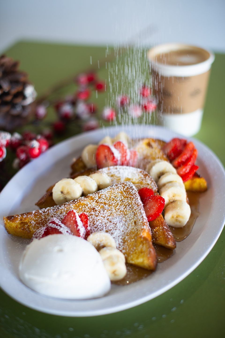 Powdered sugar sprinkles over French toast topped with strawberries, bananas, and whipped cream.