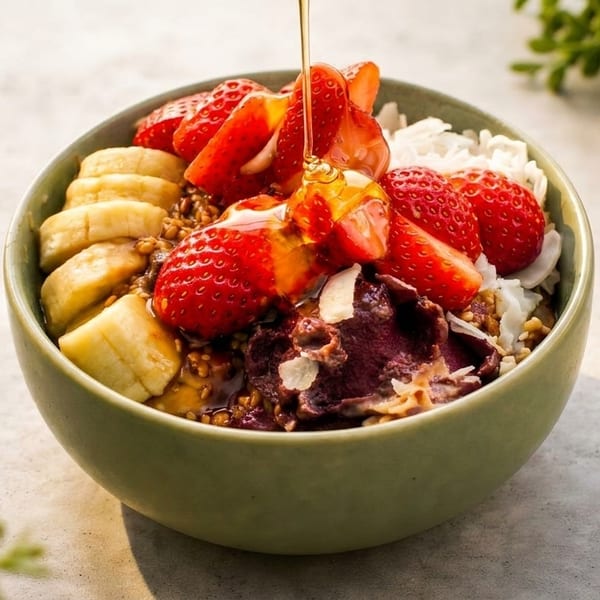 Honey drizzling over an acai bowl with strawberries, bananas, and coconut flakes.