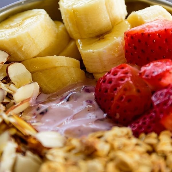 Close-up of a breakfast bowl with sliced bananas, strawberries, almonds, granola, and yogurt.