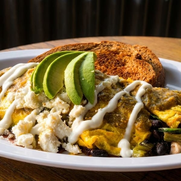 A plate of green chile omelet with avocado, feta, black beans, and toast.