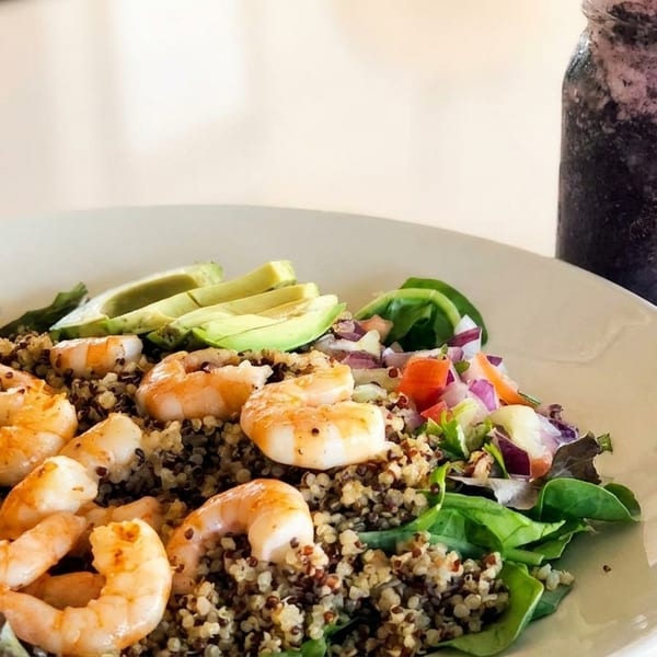 Shrimp and quinoa bowl with avocado, mixed greens, and a berry smoothie in a mason jar.