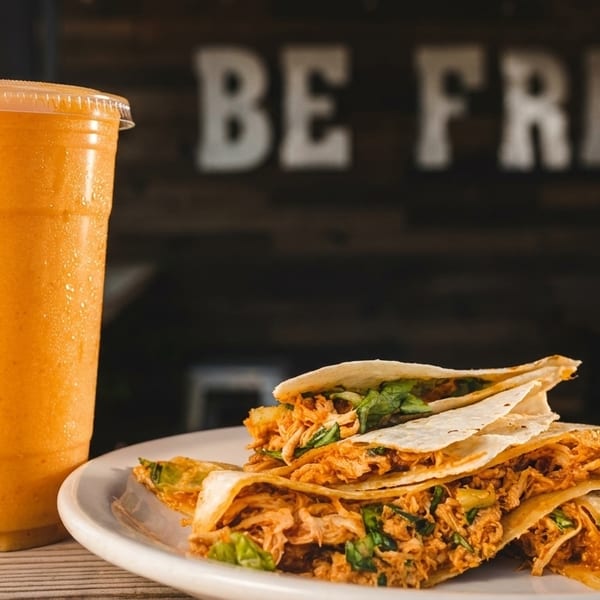 Chicken quesadillas and an orange smoothie on a wooden table with a "BE FRESH" sign.