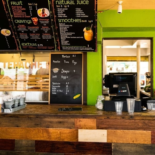 A vibrant green juice bar interior with a wooden counter, menu boards, and a person working behind the counter.