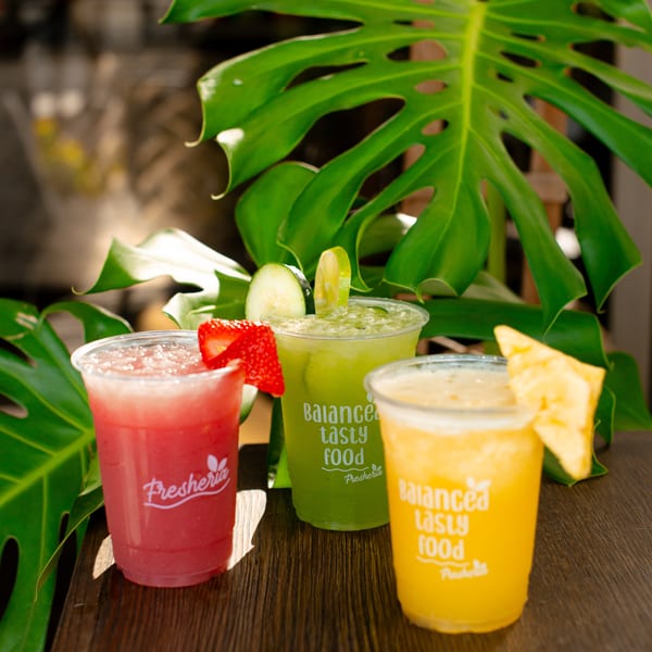 Three colorful Fresheria drinks: red with strawberry, green with cucumber and lime, and yellow with pineapple.